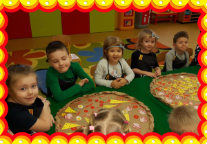 Dzieci siedzą przy stole. Przed nimi wykonane pizze.